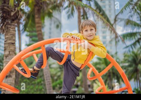 Il ragazzo sale sul parco giochi sullo sfondo di palme Foto Stock