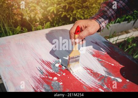 painter dipinge la superficie bianca. L'immagine è uno sfondo bianco appena dipinto e un pennello in mano su un tavolo rosso. Foto Stock
