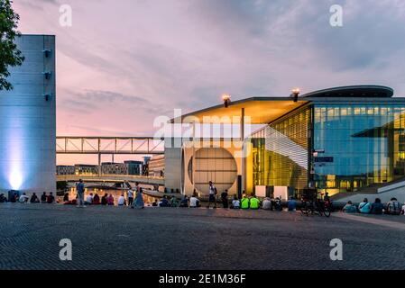 Berlino, Germania - 28 luglio 2019: Persone che siedono sulla riva del fiume accanto al complesso di edifici governativi illuminati al tramonto. Foto Stock