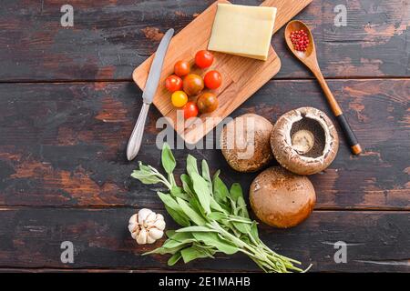 Funghi Portabello ingredienti per la cottura, formaggio cheddar, pomodori ciliegini e salvia su vecchio sfondo di legno scuro, vista dall'alto spazio per il testo Foto Stock