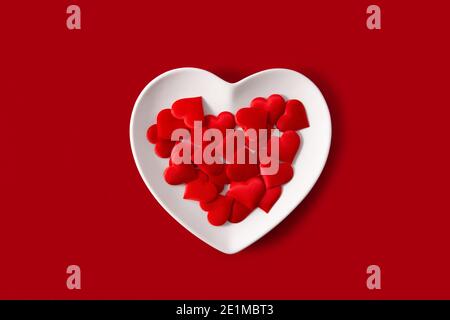 Piastra a forma di cuore con cuori rossi all'interno su sfondo rosso Foto Stock