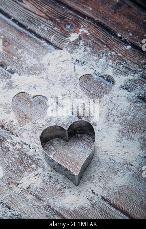 Taglierina per biscotti a forma di cuore sul tavolo da cucina e la farina. Concetto di San Valentino. Immagine verticale Foto Stock