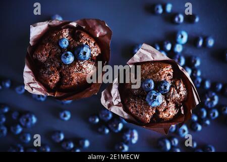 Vista dall'alto di deliziosi cupcake al cioccolato con ripieno di mirtilli, intorno ai quali si trovano bacche mature di mirtilli selvatici. Dolci. Foto Stock