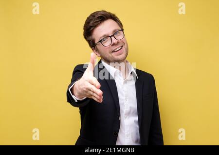 Uomo d'affari scuotendo le mani isolate sulla parete gialla. Scatto in studio Foto Stock