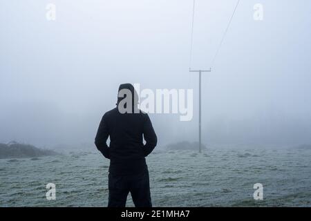 Un personaggio agganciato, torna alla fotocamera. Guardando i poli del telegrafo. In un giorno di inverni gelidi e nebbie. Foto Stock