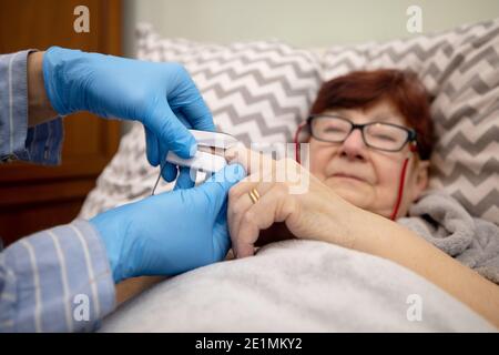 Test ossimetrico paziente anziano nella prevenzione della polmonite da Covid 19 in una casa di cura , medico che esamina la donna anziana utilizzando ossimetro a casa Foto Stock