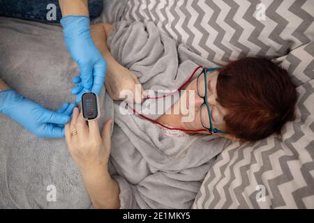 Test ossimetrico paziente anziano nella prevenzione della polmonite da Covid 19 in una casa di cura , medico che esamina la donna anziana utilizzando ossimetro a casa Foto Stock