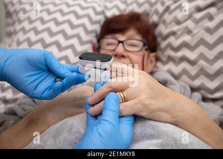 Test ossimetrico paziente anziano nella prevenzione della polmonite da Covid 19 in una casa di cura , medico che esamina la donna anziana utilizzando ossimetro a casa Foto Stock