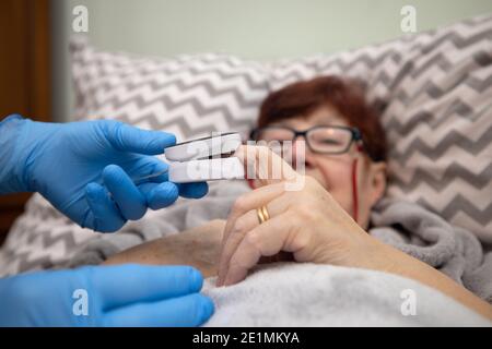 Test ossimetrico paziente anziano nella prevenzione della polmonite da Covid 19 in una casa di cura , medico che esamina la donna anziana utilizzando ossimetro a casa Foto Stock