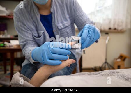 Test ossimetrico paziente anziano nella prevenzione della polmonite da Covid 19 in una casa di cura , medico che esamina la donna anziana utilizzando ossimetro a casa Foto Stock