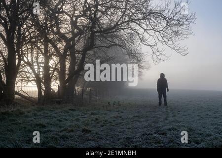 Un personaggio agganciato, torna alla fotocamera. Guardando nella nebbia. In una giornata di inverni gelidi e atmosferici in campagna. Foto Stock