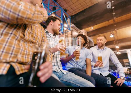 Vista dal basso di quattro amici maschi che parlano e bevono birra al pub. Foto Stock