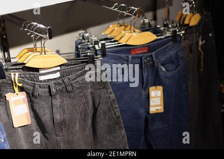 Fila di jeans blu e neri impiccati su grucce di legno in un negozio. Foto Stock