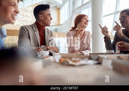 Un gruppo di dipendenti che si sono bene in un'atmosfera allegra in una pausa presso la mensa dell'azienda. Persone, lavoro, azienda, business concept. Foto Stock