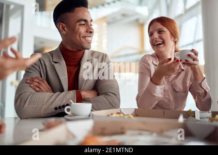 Un gruppo di dipendenti in una pausa gustando un caffè e chiacchierando in un'atmosfera allegra presso la mensa dell'azienda. Persone, lavoro, azienda, business concept. Foto Stock