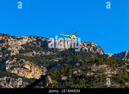 Elicottero che trasporta acqua per mettere fuori un fuoco di foresta dentro La catena montuosa della Serra de Tramuntana nel nord-ovest di Maiorca Isole Baleari Spagna Foto Stock