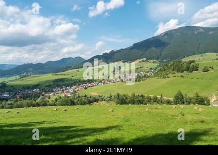 Vista sul villaggio di Liptovska Luzna ai piedi delle montagne di Low Tatra con prati verdeggianti, colline boscose e balle di paglia. Slovacchia, estate Foto Stock