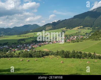 Vista sul villaggio di Liptovska Luzna ai piedi delle montagne di Low Tatra con prati verdeggianti, colline boscose e balle di paglia. Slovacchia, estate Foto Stock