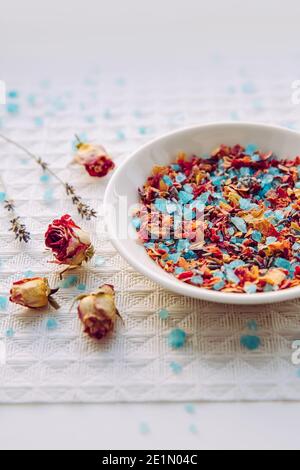 Petali di rosa secchi fatti in casa bagno di fiori miscela di sale per aromaterapia e relax nella vasca da bagno, mix bagno. Piatto con sale da bagno di colore blu mescolato. Foto Stock