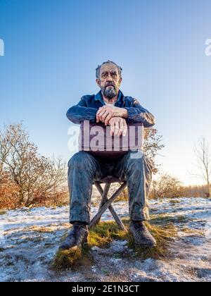 Vista frontale della figura seduta di Sean Henry. Scultura in grande scala in un parco di sculture dello Yorkshire innevato. Foto Stock