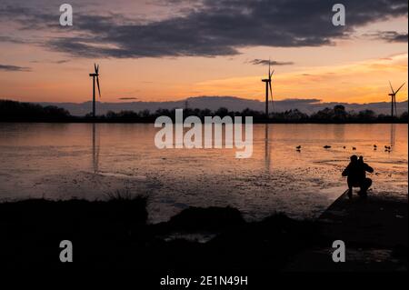 Ombra di giovane maschio che si affaccia lago congelato con bambino con turbine in background duing tramonto. galles del sud uk. Foto Stock