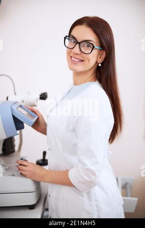 Bel medico degli occhi sorridente mentre si utilizza un rifrattometro automatico Foto Stock