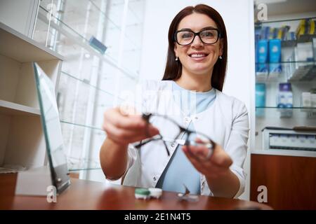 Medico femminile che tiene fuori gli occhiali ad un ospite Foto Stock