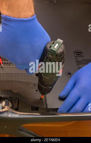 Un tecnico del centro di assistenza svita il pannello posteriore di un televisore LCD utilizzando un cacciavite. Mani in guanti primo piano, messa a fuoco selettiva. Foto Stock