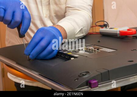 Il tecnico del centro di assistenza rimuove il pannello posteriore dal LED del monitor TV per la riparazione. Cacciavite a mano con guanti. Primo piano, messa a fuoco selettiva, sfocatura. Foto Stock