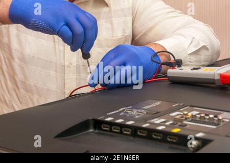 La riparazione del televisore LCD, il tecnico dei guanti con un cacciavite rimuove il pannello posteriore del monitor. Messa a fuoco selettiva, primo piano. Foto Stock