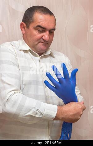 L'uomo caucasico mette un guanto di stoffa blu sulla sua mano, si prepara al lavoro. Concetto di protezione delle mani, protezione della salute. Foto Stock