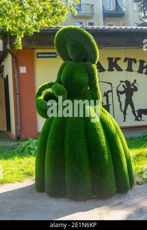 Pionersky, Regione di Kaliningrad, Russia - Settembre, 2020: Figura arbusto di signora in abito lungo e cappello fatto di erba verde. Topiario urbano. Foto Stock