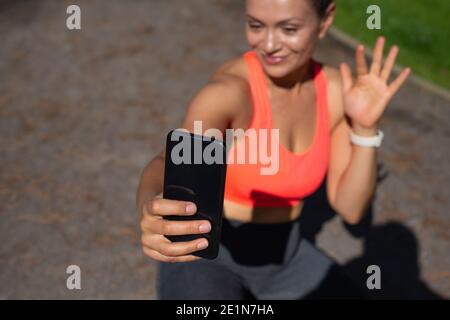 Concentratevi sullo smartphone nero in una mano sorridente di una donna seduta in corsa Foto Stock