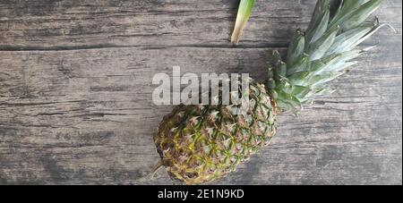 Un ananas intero adagiato su un tavolo di legno Foto Stock