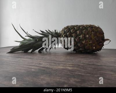 Un ananas intero adagiato su un tavolo di legno Foto Stock