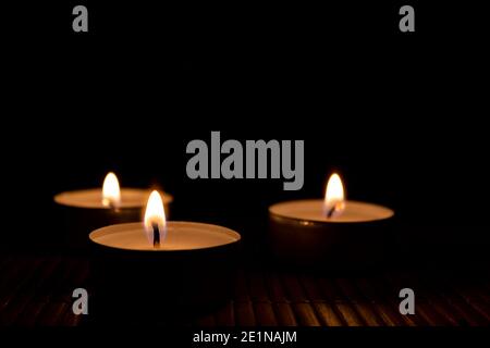 Tre candele che bruciano, primo piano e fuoco selettivo sul primo piano. Candele al buio con spazio di copia per il testo Foto Stock