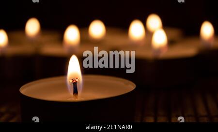 Primo piano di candele bruciate al buio con otto candele sfocate nel backgorund. Sfondo astratto candele Foto Stock