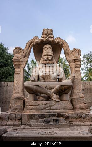 Hampi, Karnataka, India - 5 novembre 2013: Tempio Lakshmi Narasimha. Gigantesca statua di pietra marrone del dio sotto il cielo blu con fogliame verde sul retro. Foto Stock