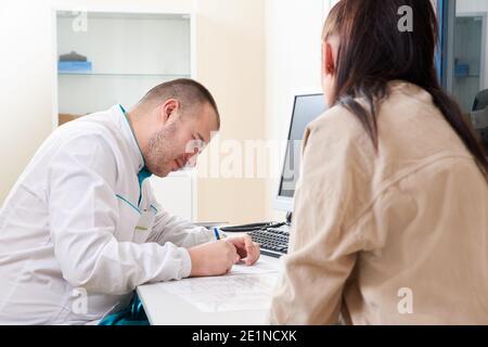 Giovane medico di sesso maschile che esamina e consulta la giovane paziente femminile in clinica ospedaliera. Medico professionista medico generico diagnosi medico Foto Stock