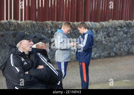 Due giovani ragazzi, ragazzi in una partita di calcio locale a Irvine, Ayrshire, Scozia, Regno Unito. Controllare i loro telefoni cellulari in primo piano due anziani supportati in matching treack tute Foto Stock