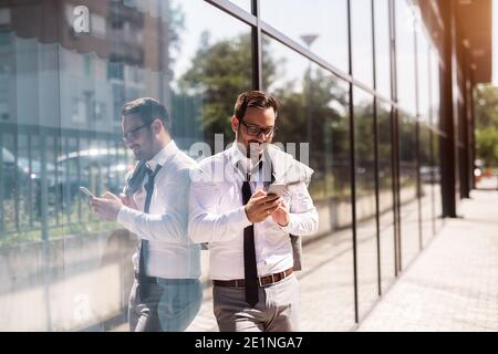 Dopo aver terminato una giornata di lavoro difficile, il giovane uomo d'affari si trova fuori e invia messaggi alla moglie. Foto Stock