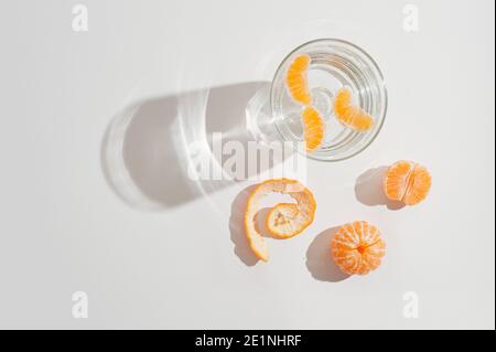 Acqua cristallina in vetro trasparente con fette di mandarino fresco su sfondo bianco. Disposizione piatta minima. Foto Stock