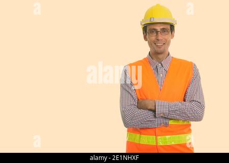Studio shot del giovane uomo felice lavoratore edile sorridente indossando occhiali con le braccia incrociate Foto Stock