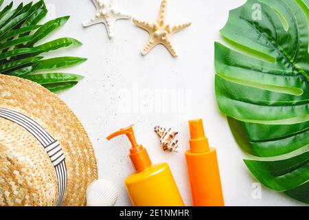 Bottiglie di crema solare disposte con cappello di paglia su sfondo bianco con foglie di palma, vista dall'alto Foto Stock