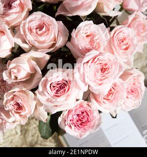 Rosa Bianco Rosa o'hara. Bouquet di rose rosa in vaso di vetro con una teiera bianca e due tazze di cappuccino su un vassoio su un tavolino tra i libri. Foto Stock