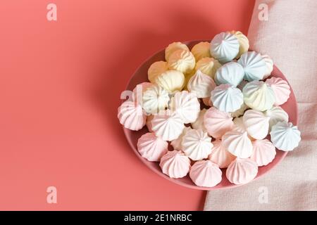 Dessert multicolore con proteine dello zucchero in colori pastello in un piatto rosa su sfondo rosa. Tovagliolo di lino. Copia spazio Foto Stock