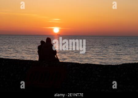 Coppia guardando il sole tramontare sul mare a Brighton, East Sussex, Inghilterra, Regno Unito Foto Stock