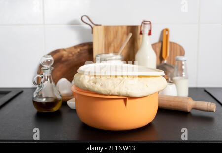 la pasta di lievito pronta per preparare panini fatti in casa si trova sul tavolo tra gli altri ingredienti per la cottura del pane. Foto Stock