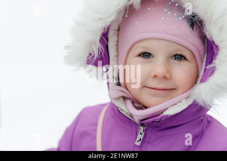 Ritratto di una bambina sorridente in un cappuccio rosa sulla strada contro uno sfondo di neve Foto Stock