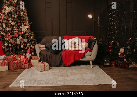 Un giovane si addormentò sul divano vicino all'albero di natale. Mattina di Natale. Appartamento interno. San Valentino cel Foto Stock